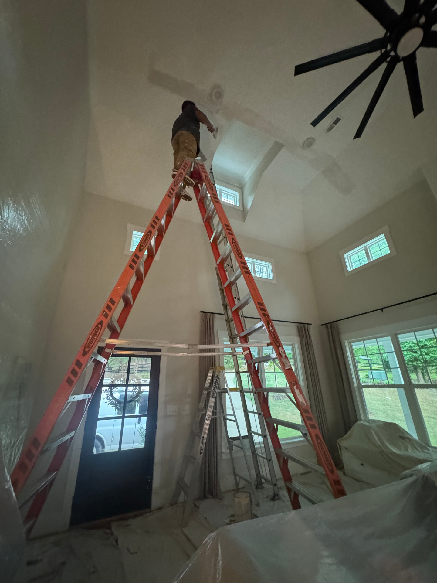 Painter on tall ladder finishing a two-story vaulted ceiling